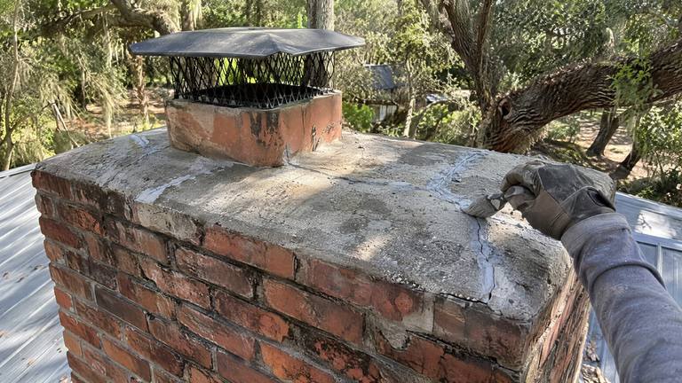 A gloved hand works gray crack sealant into a cracked concrete crown with a small brush.