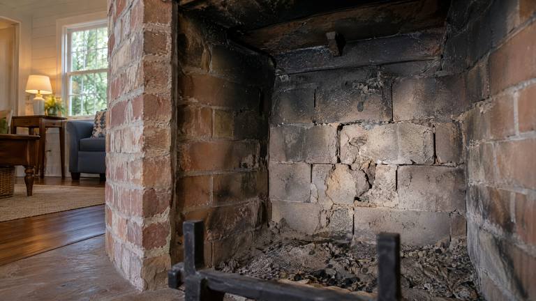 Cracked and spalled firebricks with open joints on the back wall of an old sooty firebox, seen past the grate.