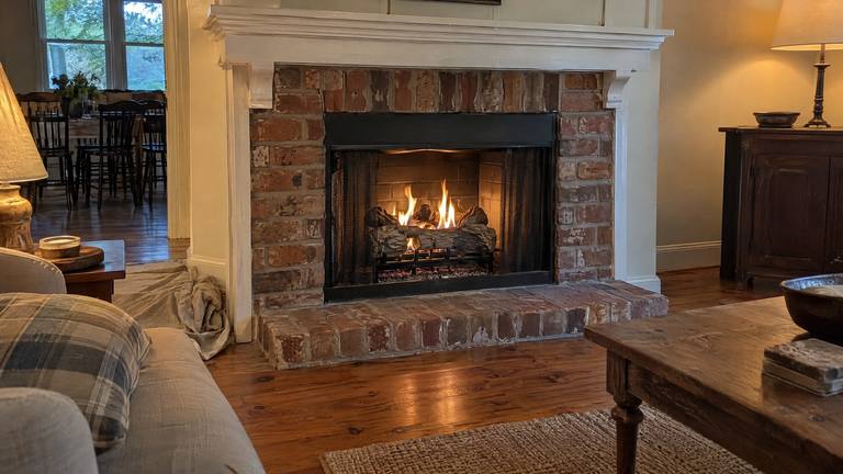 A newly installed gas log set burns with calm flames in an older orange-red brick fireplace.