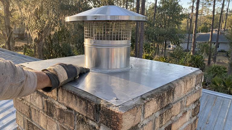 A stainless top plate sealed on a tan brick chimney crown with a new liner and rain cap.