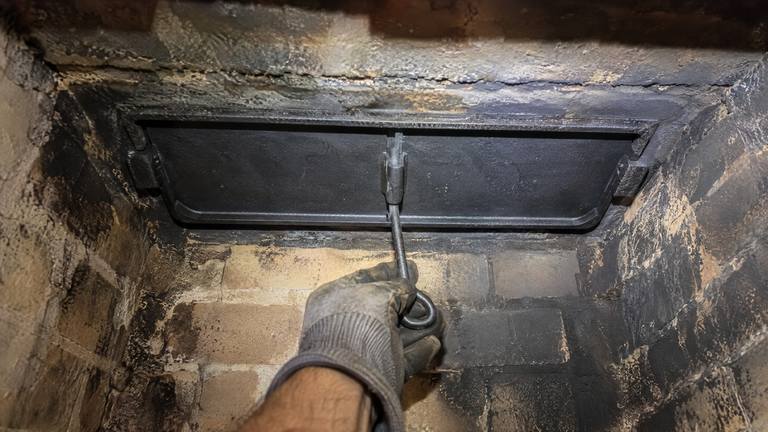 A new cast-iron damper plate sits closed in the throat of a tan brick firebox, its handle below.