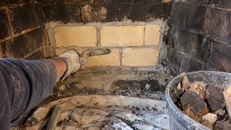 Pale new firebricks are set in fresh mortar in the sooty back wall of a firebox.