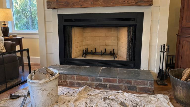 A factory-built fireplace with clean new tan refractory panels inside and the old broken pieces in a bucket in front.