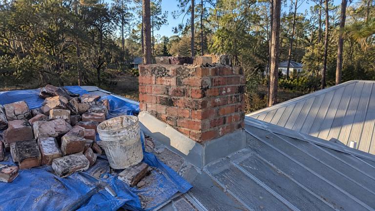 Old bricks from a chimney taken down near the roofline are piled on a blue tarp on a metal roof.