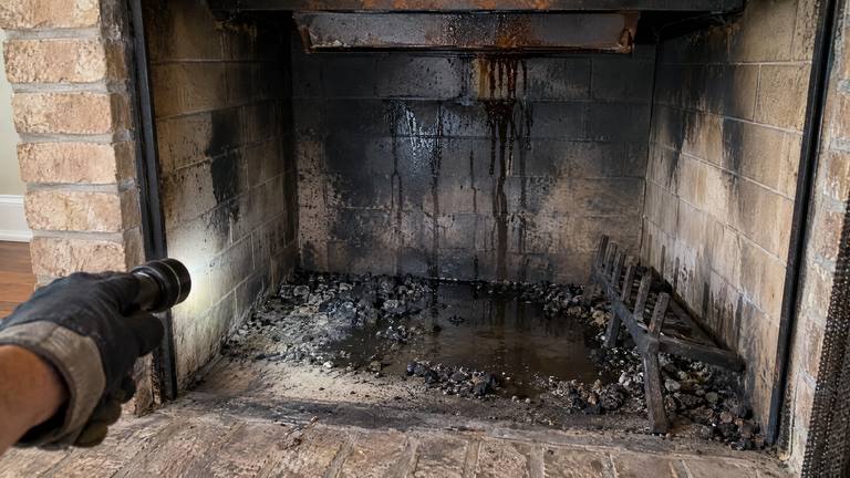 Rainwater stands on the floor of a sooty firebox, with drip streaks running down the back wall.