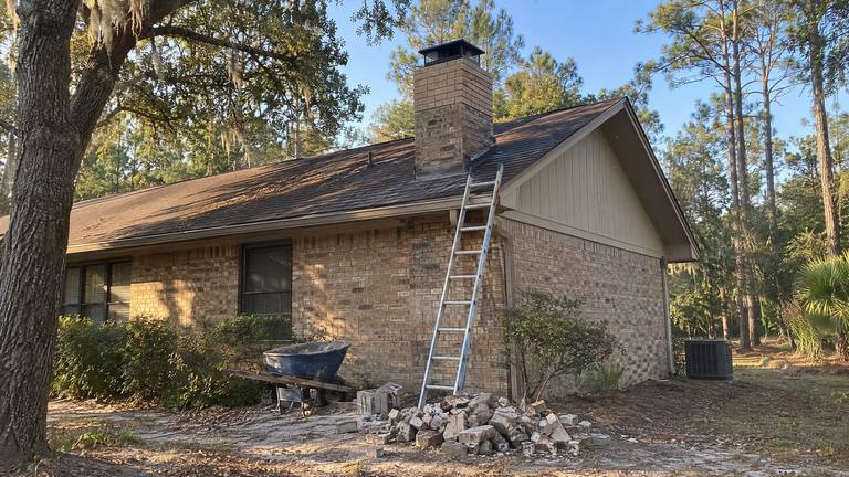 A tan brick ranch home whose chimney top has been rebuilt in newer brick with a fresh crown and cap.