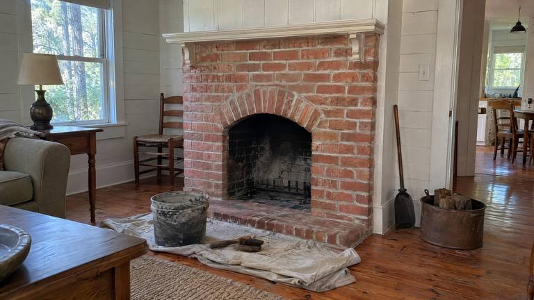 A restored older brick fireplace with clean repointed joints and a simple wooden mantel in a farmhouse room.