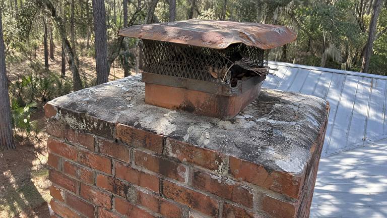 An old rusted chimney cap with a torn screen and twigs caught in it sits on a clay flue.