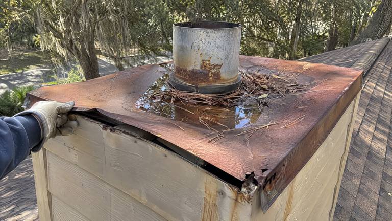 An old chase cover rusted through and sagging in the middle, with water pooled around the flue pipe.
