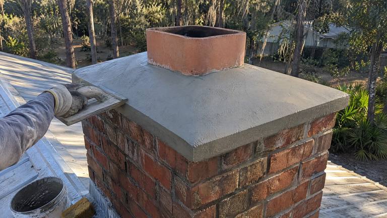 A freshly cast concrete crown with a sloped top and an overhang on an orange-red brick chimney.