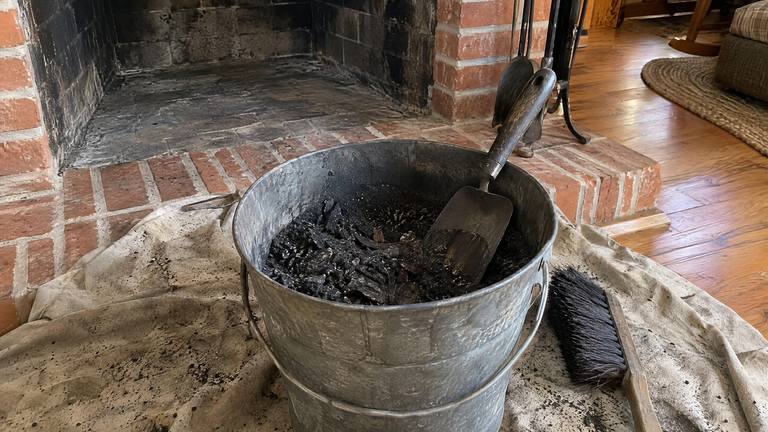 A metal bucket of black soot and creosote flakes sits on a drop cloth beside a swept fireplace.