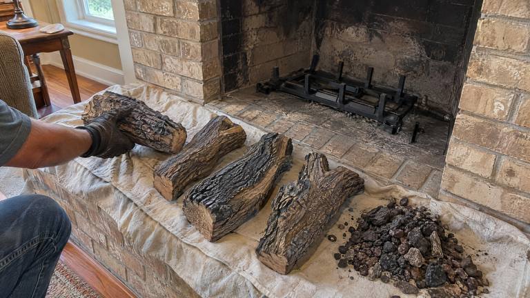 New ceramic gas logs and ember rock are laid out on a drop cloth on the hearth beside an empty burner grate.