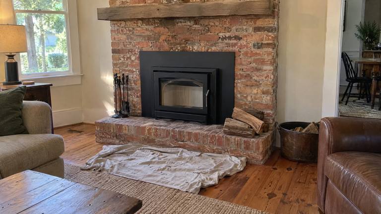 A new black wood insert with a glass door fills an older orange-red brick fireplace.