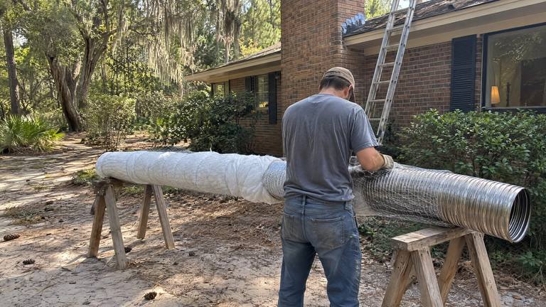 A stainless steel chimney liner laid on sawhorses in a driveway is wrapped with an insulation blanket.